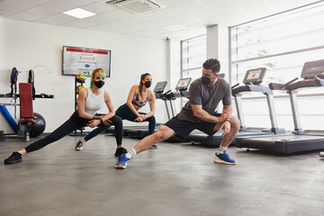 Fototapeta na wymiar Healthy fit group of people stretching, wearing masks in gym