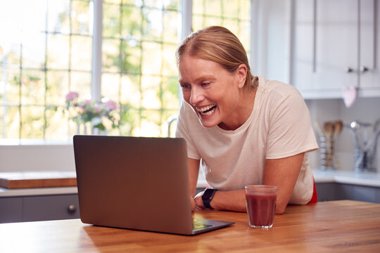 Mature Woman Wearing Fitness Clothing At Home Logging Activity From Smart Watch Onto Laptop - Powered by Adobe