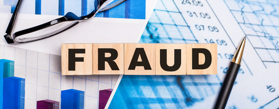 On the bright diagrams, glasses, a pen and wooden cubes with the word FRAUD. Business concept