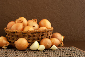 Basket with onions on a brown background. Lots of onions in a basket on a bamboo napkin. Onions and space for text. Vegetables on a textured background.