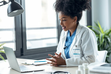 Attractive afro female doctor talking while explaining medical treatment to patient through a video call with laptop in the consultation.