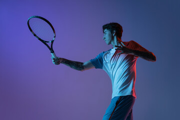 Fototapeta na wymiar Young caucasian man playing tennis isolated on purple-blue studio background in neon, action and motion concept