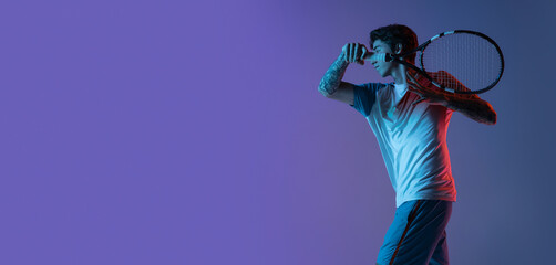 Young caucasian man playing tennis isolated on purple-blue studio background in neon, action and motion concept