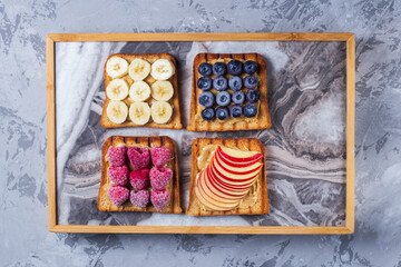 Toasted sandwich bread with peanut butter, banana, frozen berries raspberries, blueberries. Served on concrete background. Healthy, balanced traditional breakfast. Vegan sweet dessert, top view