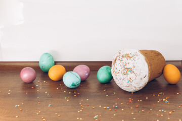 Easter cake with scattered sprinkles on a wooden table, and Easter eggs of different colors - yellow eggs, green and purple eggs. Easter eggs and cake with scattered sweets.