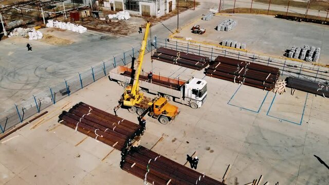 The working process in a warehouse with a metal. Workers unload a metal in a truck standing under a gantry crane. Transportation. Industry. Oil industry. Pipe production. Drilling rig.