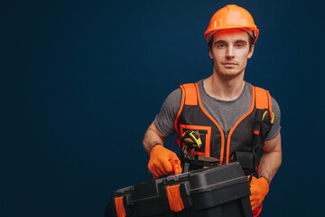 Serious young builder is holding equipments, isolated on blue background.