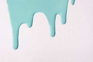 Light cyan liquid drops of paint color flow down on isolated white background. Abstract turquoise backdrop.