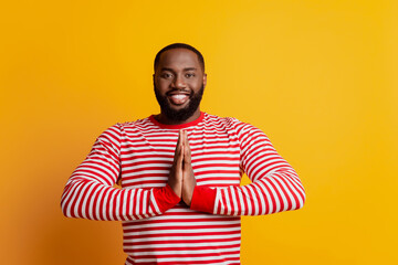 Young man make pleading gesture hold palms together on yellow wall