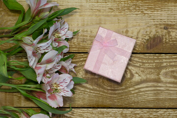 Bright white and pink flowers Alstroemeria and pink paper wrapped gift box on wooden textured background close-up