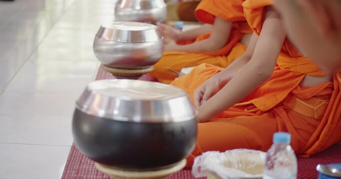 The novices and the monks sit and prepare to pray before eat food in their alms bowls after people made merit at Buddhist temple.
