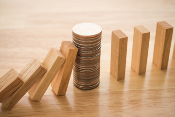 Stacked coins stop wood block fall domino effect on office wooden table background. Money cash for save business from economy crisis. Banking, business and financial concept.