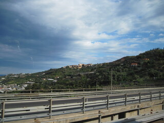 clouds over the forest. Car driving on a highway. Cars on the road in the Alps mountains on a cloudy summer day. Scenic view with autobahn traffic and morning blue sky.