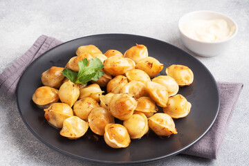 Traditional fried pelmeni, ravioli, dumplings filled with meat on black plate, russian kitchen. Gray concrete background, copy space.