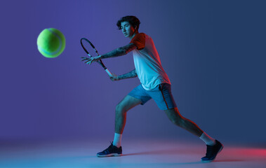 Young caucasian man playing tennis isolated on purple-blue studio background in neon, action and motion concept