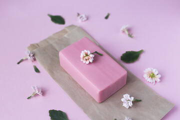 Natural soap for the body, face in a paper bag packed near flowers on a pink background.