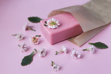 Natural soap for the body, face in a paper bag packed near flowers on a pink background.