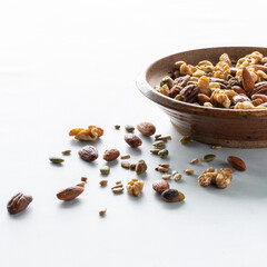 A bowl full of trail mix with several nuts scattered in front.