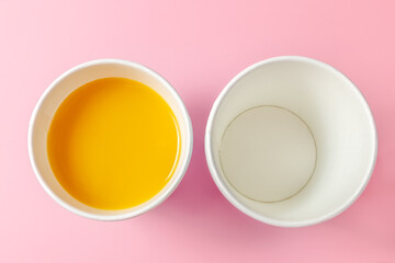 Disposable paper cup and orange juice on a pink background. Disposable tableware. Disposable goods. Concept. View from above.