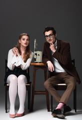 worried couple in retro outfit watching movie on film projector on grey background
