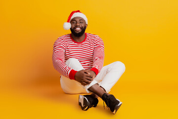Portrait of positive guy in santa hat sit floor isolated on yellow background