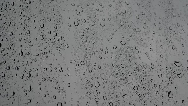 4K Droplets on glass car window in rainy day in white dark background with copy space. Concept of rainy season.