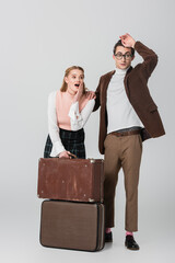 shocked retro style couple looking away near suitcases on grey background