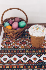 Ukrainian embroidered shirt and Easter cake on a wooden table with Easter eggs of different colors - yellow eggs, green and purple eggs in a basket.Easter eggs and Easter cake on an embroidered towel.