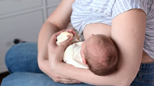 Mother breastfeeding a baby. Maternity love, babycare concept. Woman breastfeeding her newborn baby at home. Peaceful loving young mother sitting on bed while feeding baby with breast.