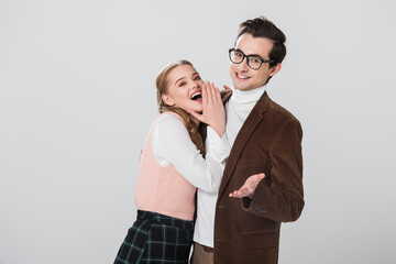 excited woman covering open mouth near cheerful man pointing with hand isolated on grey