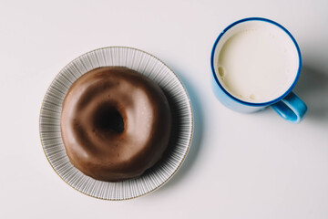Donut de chocolate fresco delicioso sobre fondo blanco. Apetitosa y sabrosa rosquilla glaseada lista para comer con una taza de leche fresca
