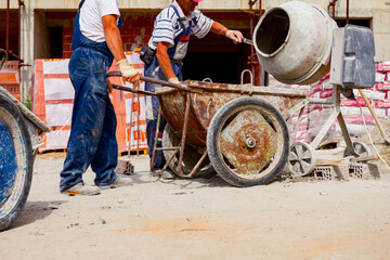 Workers are pouring concrete from cement mixer into wheelbarrow