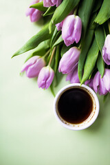 cup of coffee and purple tulips on green background