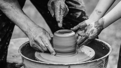 Potter teaching child to make ceramic pot on the pottery wheel. Pottery workshop outside. Potters and child hands.