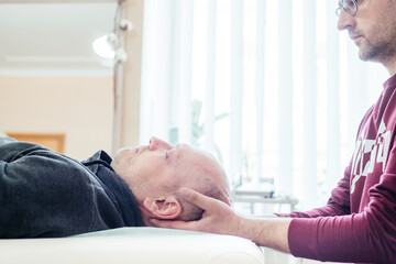 Craniosacral therapy practitioner working wiht a male patient using light touch, CST osteopathic...