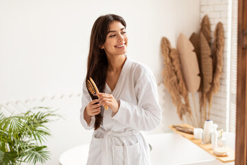 Brunette Woman Brushing Hair With Wooden Hairbrush In Modern Bathroom - obrazy, fototapety, plakaty