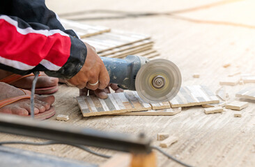 Worker in uses grinder for cutting tiles in construction site