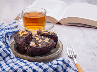Pieces of fresh brownies on a plate with a book and teacup. Side view. Delicious chocolate pie. Dessert and relaxation concept