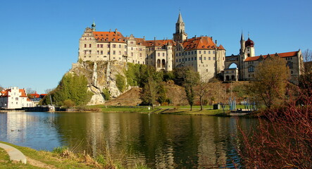 Fototapeta na wymiar herrliches Schloss Sigmaringen spiegelt sich unter blauem Himmel vor grünen Ufer der Donau mit Wehr