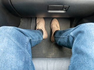 The passenger is sitting in the passenger seat of the car. The legs of a man in jeans and shoes in the interior of a car top view.