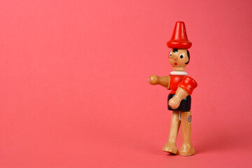 Wooden puppet depicting Pinocchio walking on a pink background