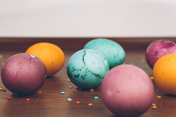 Scattered sprinkles on a wooden table and Easter eggs of different colors - yellow eggs, green and purple eggs. Easter eggs with scattered sweets.