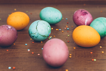 Scattered sprinkles on a wooden table and Easter eggs of different colors - yellow eggs, green and purple eggs. Easter eggs with scattered sweets.