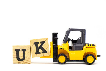 Toy forklift hold letter block k to complete word UK  (abbreviation of united kingdom) on wood background