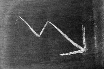 White chalk hand drawing in arrow down shape on blackboard or chalkboard background (Concept of stock decline, down trend of business, economy)