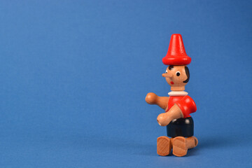 Wooden puppet depicting Pinocchio sitting on a blue background