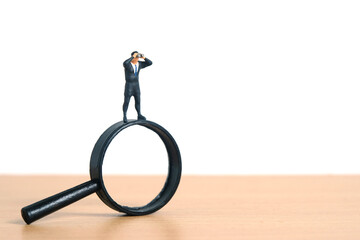Businessmen standing using binoculars above magnifying glass. Miniature tiny people toys...