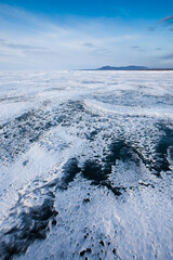Zigzag of transparent blue-turquoise ice blue sky and hills on Baikal