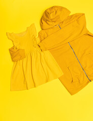 Yellow hoodie hugging a small yellow dress on a yellow background. Creative concept flat lay clothes.