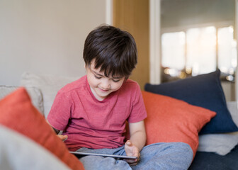 Authentic Kid sitting on sofa watching cartoons or playing games on tablet,Child boy using digital pad learning lesson on internet,Home schooling,Distance learning online education concept